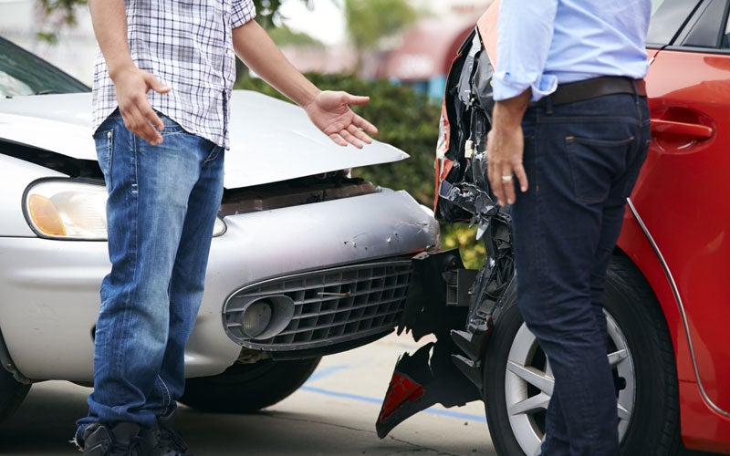Two men stand between two cars with heavily damaged front ends after a collision, one gesturing in frustration.