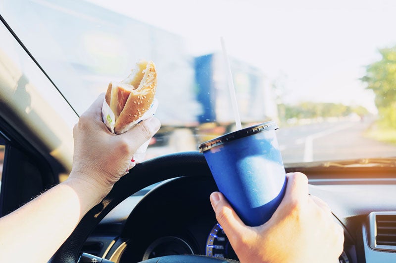 Distracted Driver holding a burger and drink while driving a car.