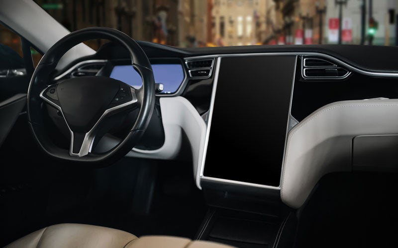 Car interior with a black steering wheel and a large vertical touchscreen display on the dashboard.