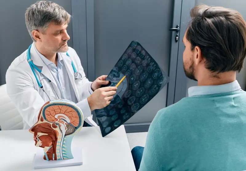 Doctor explaining brain MRI scan results to a patient, pointing at the images with a pencil.