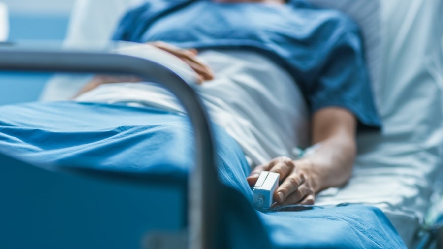 Patient in a hospital bed wearing a blue gown, with a pulse oximeter on their finger and an IV in their arm.