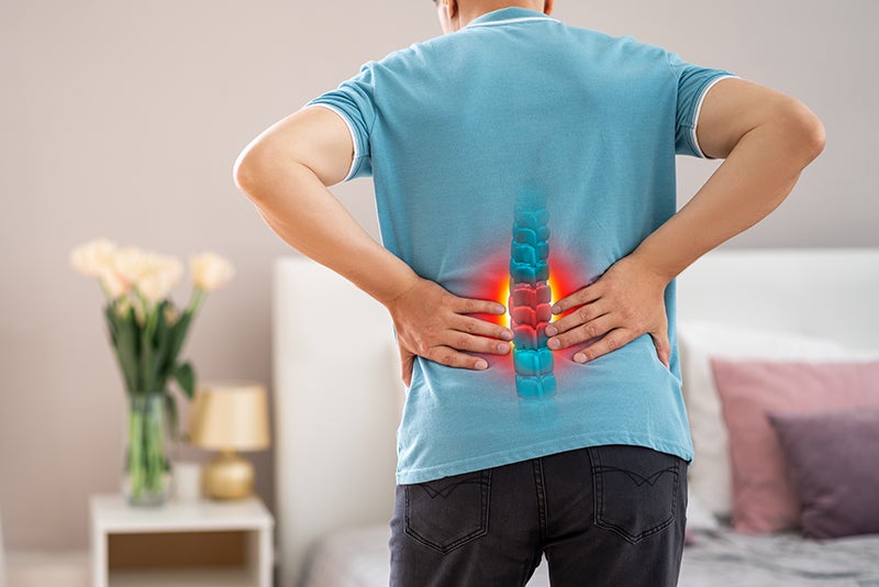 Person in blue shirt holding lower back, with glowing red and blue spine overlay highlighting lower back pain.