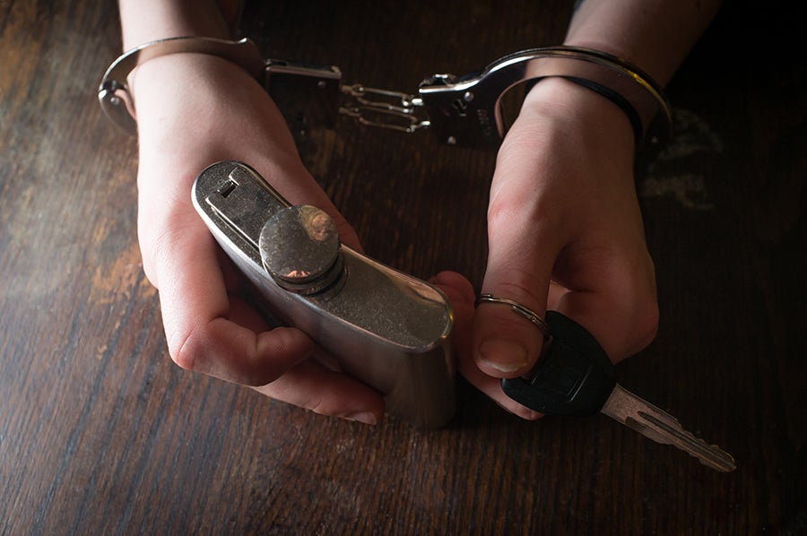 Handcuffed hands hold a metal flask and car key on a wooden surface, symbolizing drunk driving.